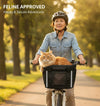 Woman cycling through a park with a ginger cat riding in the Goodsible pet bike basket on her handlebars